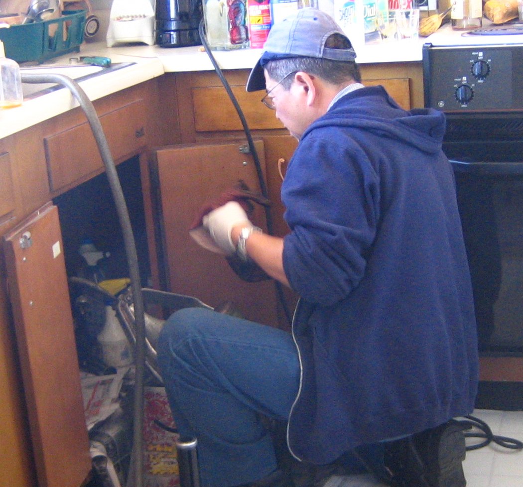 Plumber clearing a kitchen drain with a drain machine